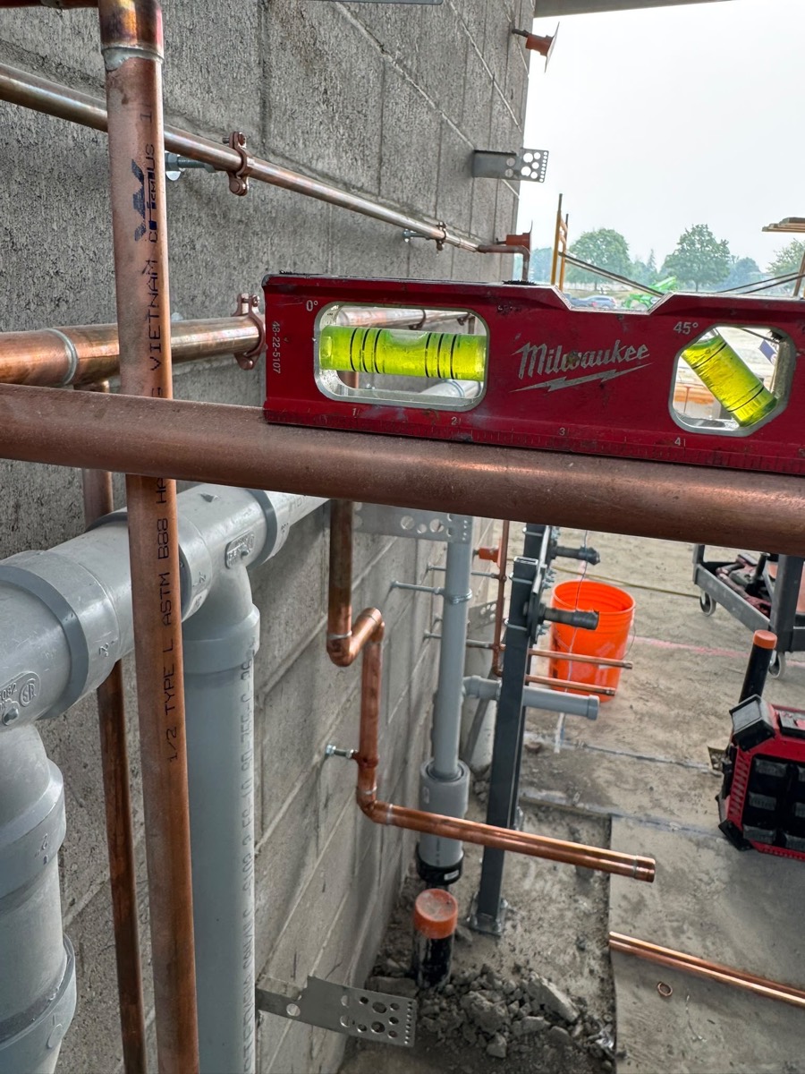 New copper riser piping being set level against a block wall
