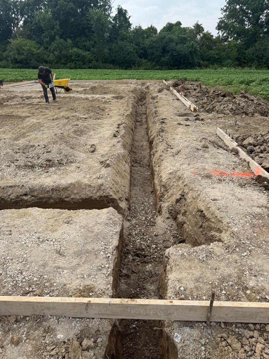 Excavated trench on a rural building lot with the crew working behind